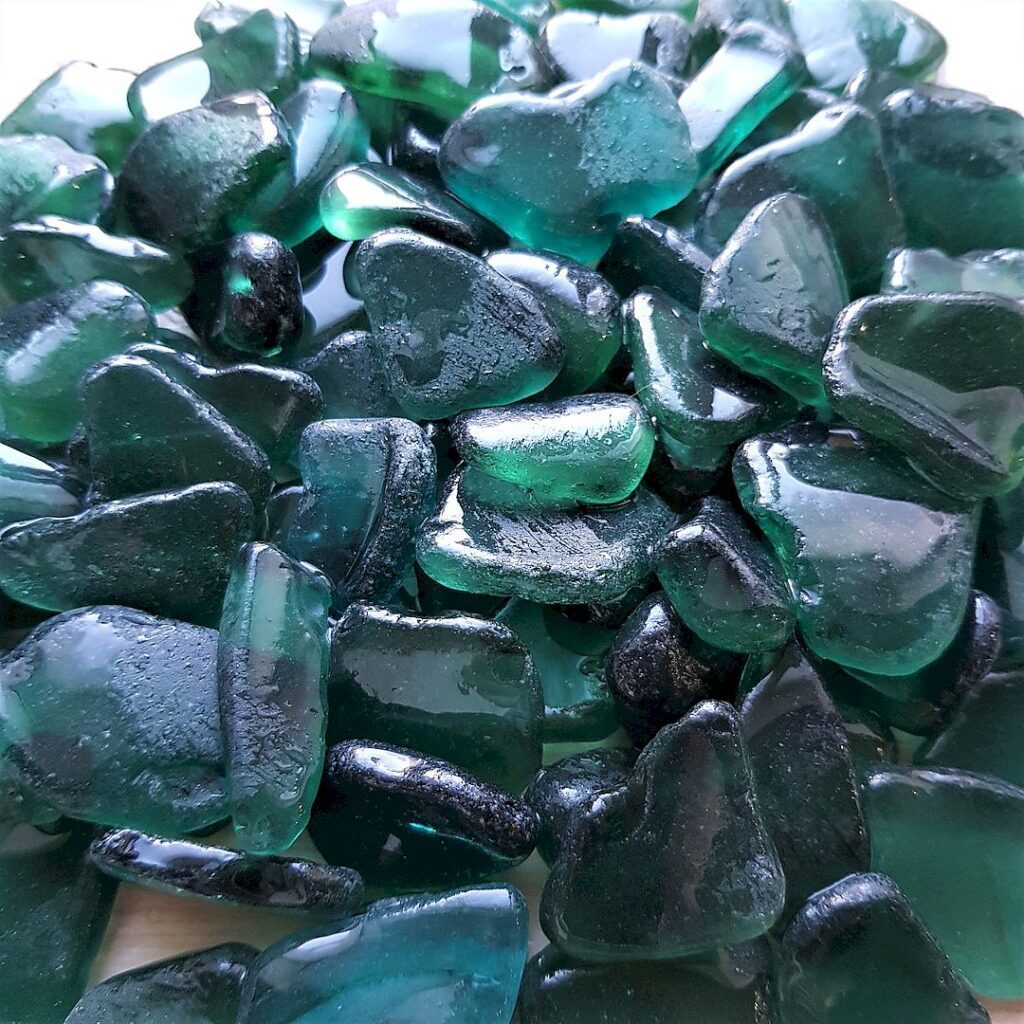 An artistic arrangement of wet large teal sea glass pieces on a neutral background.
