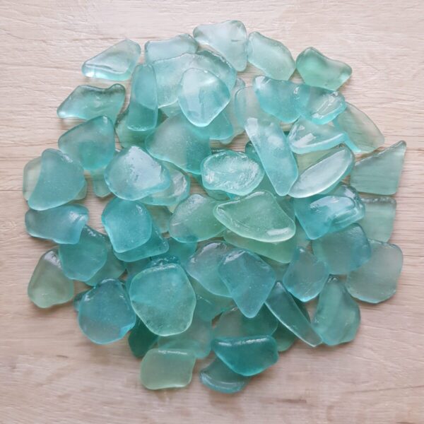 A collection of wet sea foam sea glass pieces arranged on a wooden background.