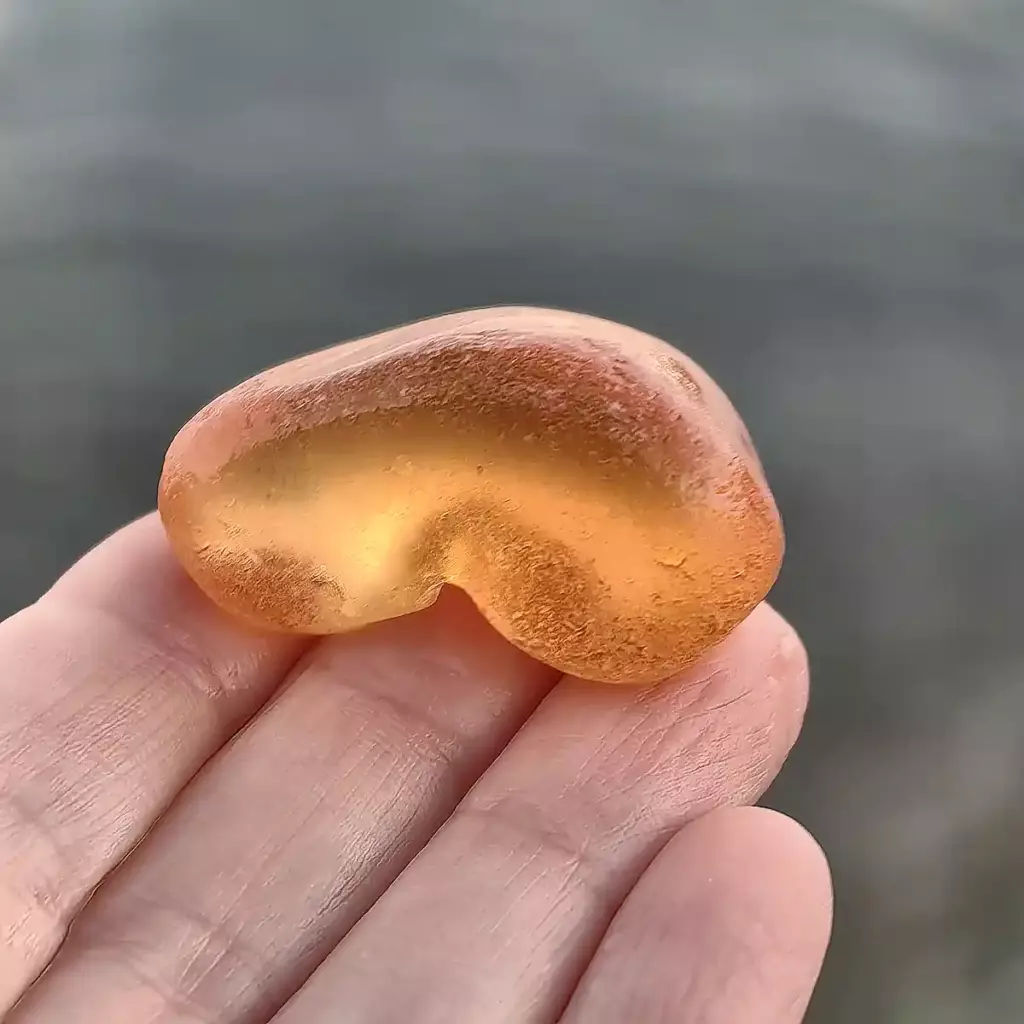 Amber orange sea glass displayed on a hand