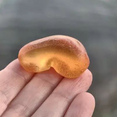Amber orange sea glass displayed on a hand